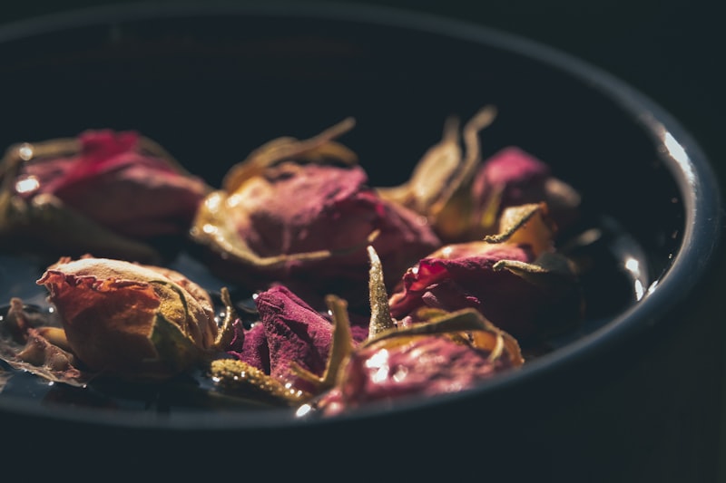A dark ceramic bowl filled with dried pink Damask rose buds, softly lit