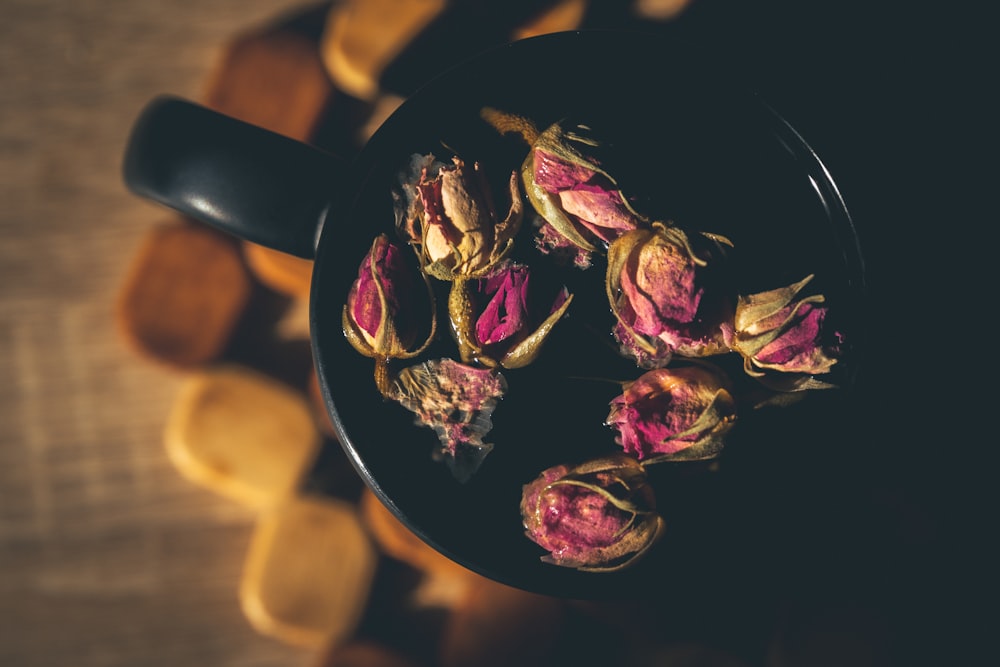Dried pink Damask rose buds arranged in a dark cup on a wooden surface