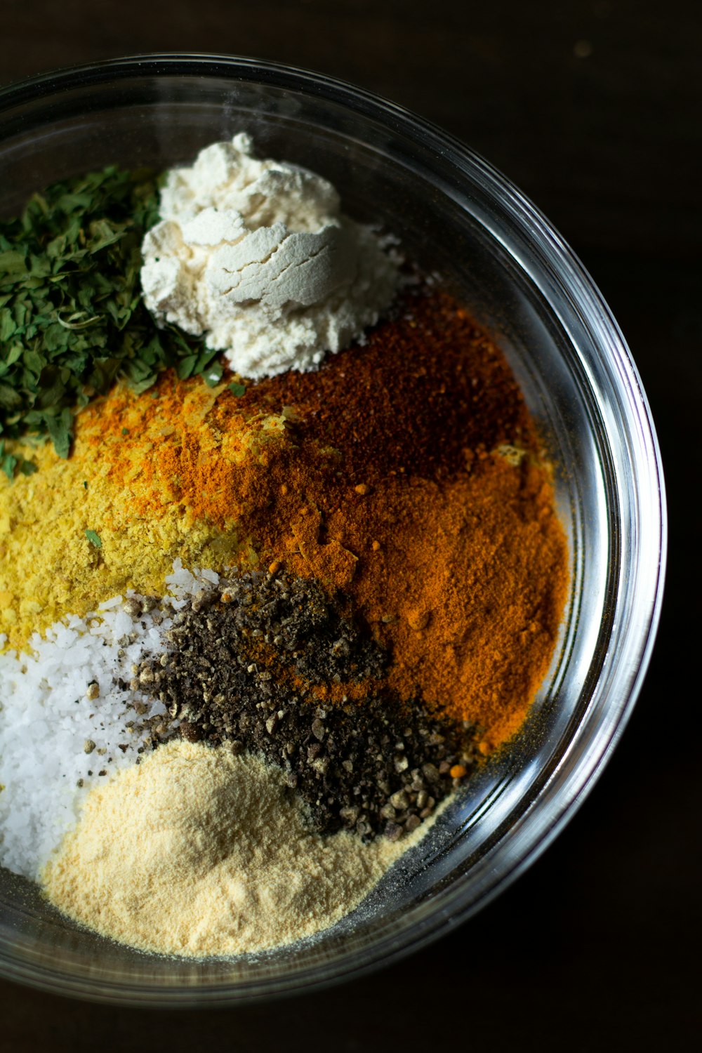 A glass bowl filled with mounds of sumac, turmeric, parsley, salt and pepper spices