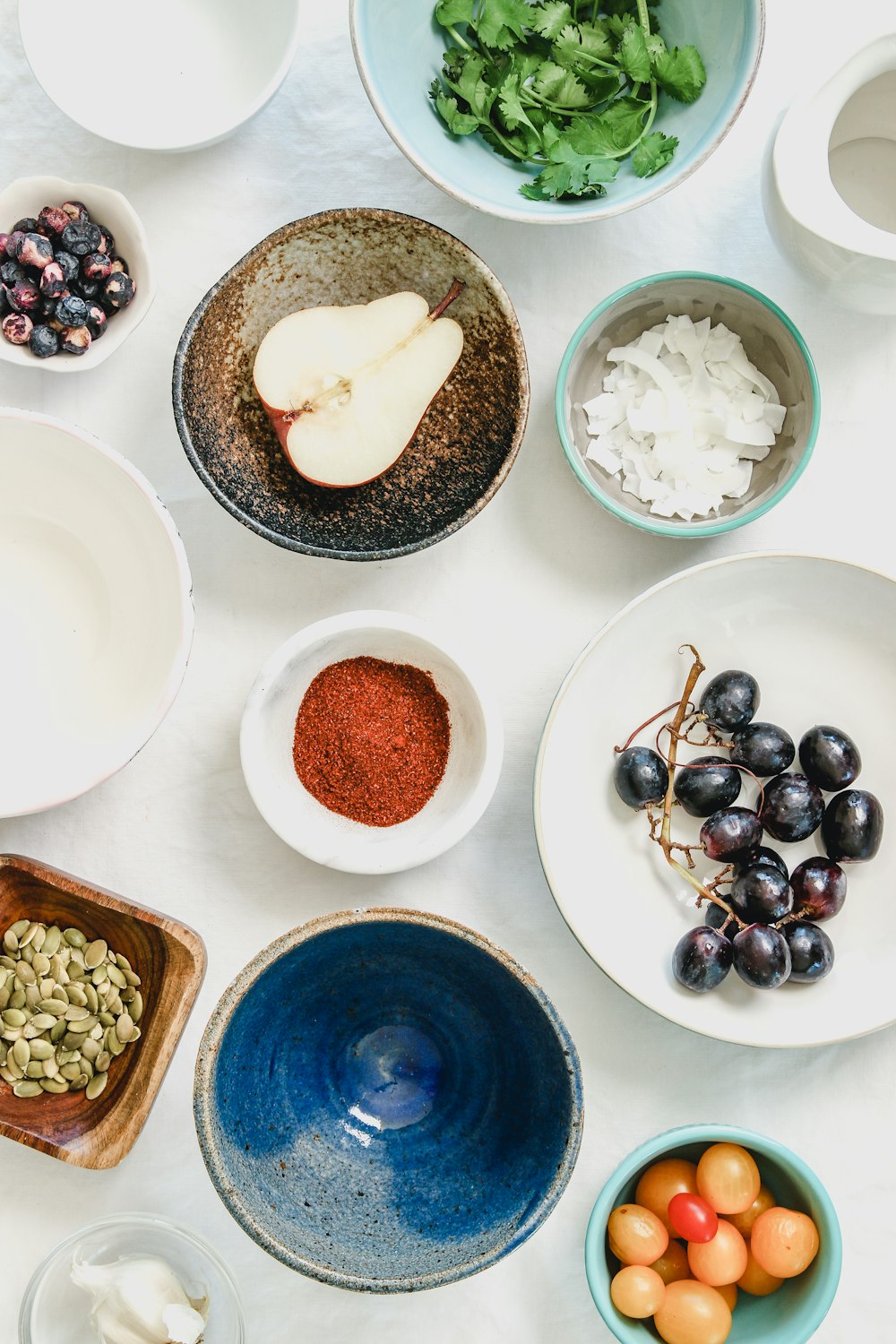 Overhead view of bowls containing sumac, coconut flakes, pumpkin seeds and other spice ingredients on a table
